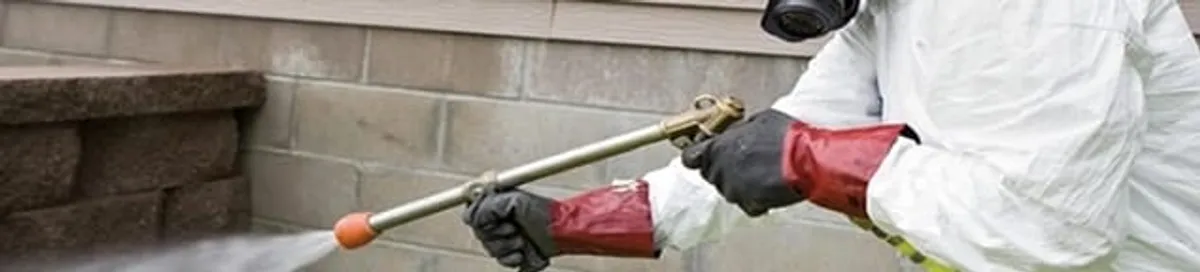 Pest control technician applying exterior insect treatment along a home foundation in Springfield, MO