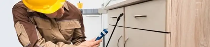 Roach exterminator applying treatment under kitchen cabinets in Springfield, MO