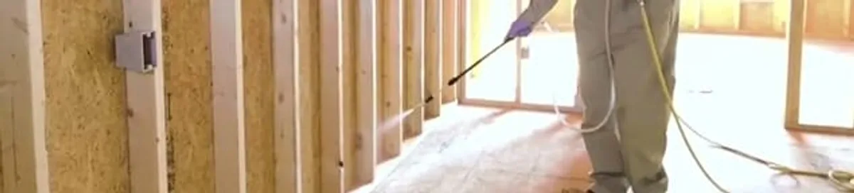 Termite treatment technician applying spray along framing and unfinished walls in Springfield, MO