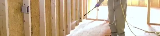 Termite treatment technician applying spray along framing and unfinished walls in Springfield, MO